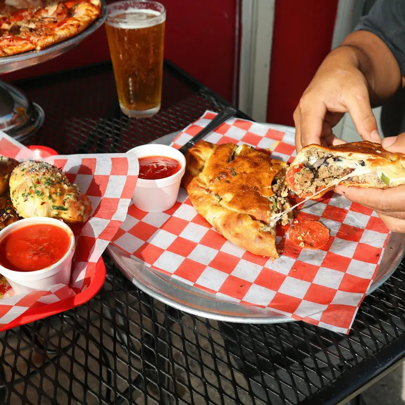 A calzone cut open next to marinara and a cold beer on a checkered basket