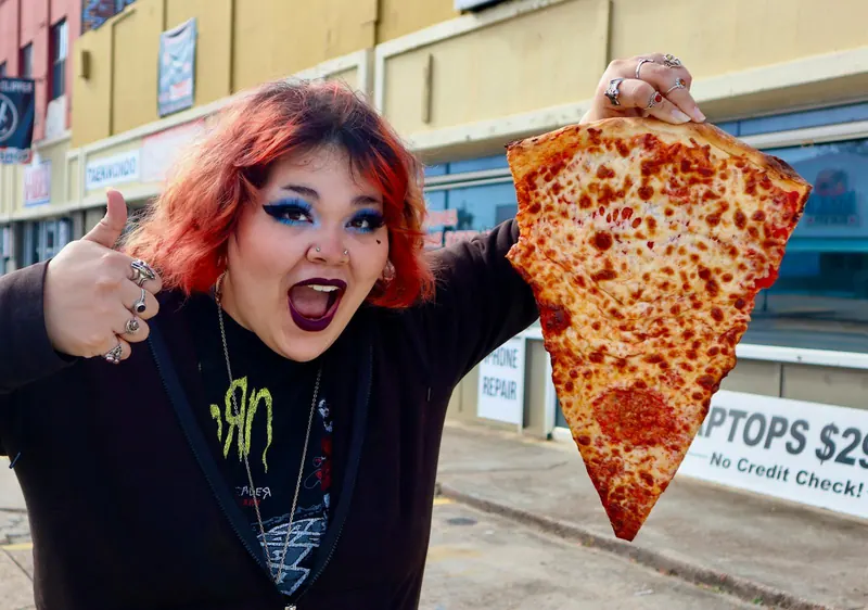 A guest holding up a cheese slice nearly the size of her torso outside Decent Pizza